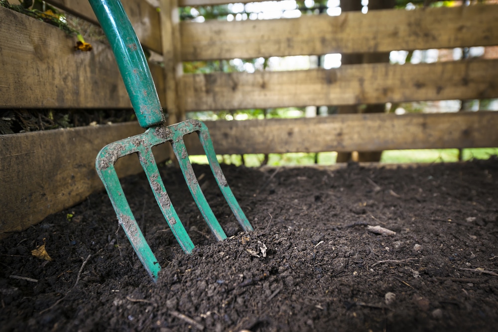 green garden fork in clean soil surrounded by fencing